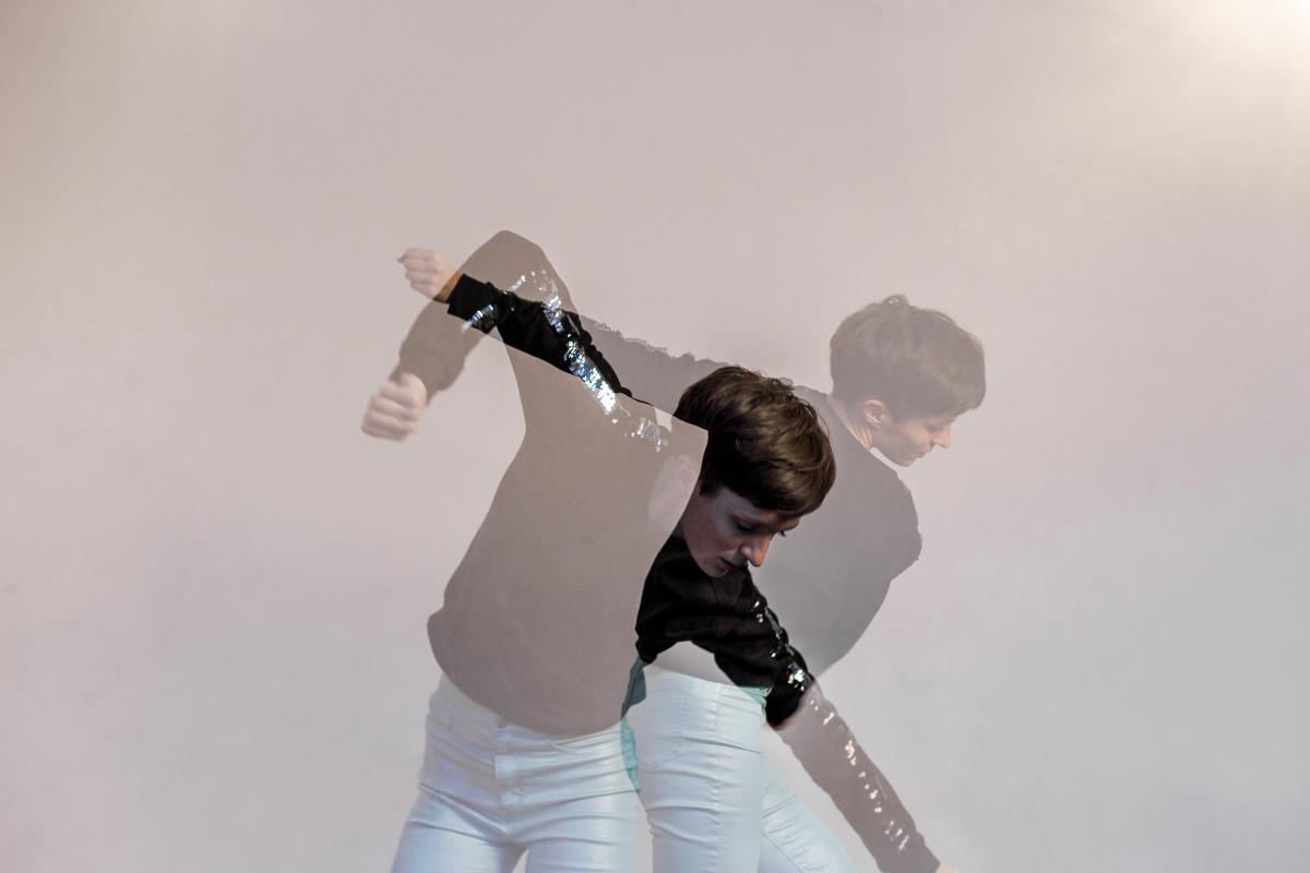 Ein konzeptionelles Bild einer Person in Bewegung, mit überlappenden Silhouetten dargestellt. Die Figur trägt ein schwarzes Oberteil und hellblaue Hosen und erscheint in mehreren verblassten Positionen, was Bewegung oder einen zeitlichen Schichteffekt suggeriert. Der neutrale Hintergrund unterstreicht die ätherische und dynamische Wirkung des Bildes.