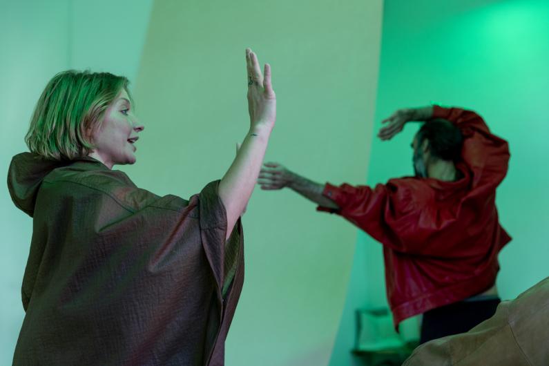 Two people move with raised arms in a room lit in green, the scene calm and focused.