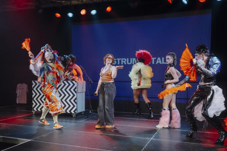 Several performers move dynamically across the stage, some with fans or elaborate costumes, while one person dances at the centre.