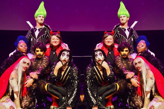 Gruppenporträt von sechs Personen auf einer Bühne, inszeniert wie ein Show-Finale. Die Personen tragen auffällige Kostüme, Make-up und Perücken in kräftigen Farben, darunter Glitzer, Spitze und ein leuchtend grüner, hochgestylter Haarschopf. Einige Personen knien oder sitzen im Vordergrund, andere stehen dahinter. Die Posen sind selbstbewusst, spielerisch und expressiv. Violettes Bühnenlicht verstärkt die theatralische, queere Ästhetik der Szene. Das Foto ist doppelt und gespiegelt.