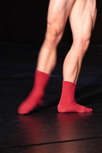 Nahaufnahme von Beinen in roten Socken. Die Person bewegt sich über eine schwarze Bühne.