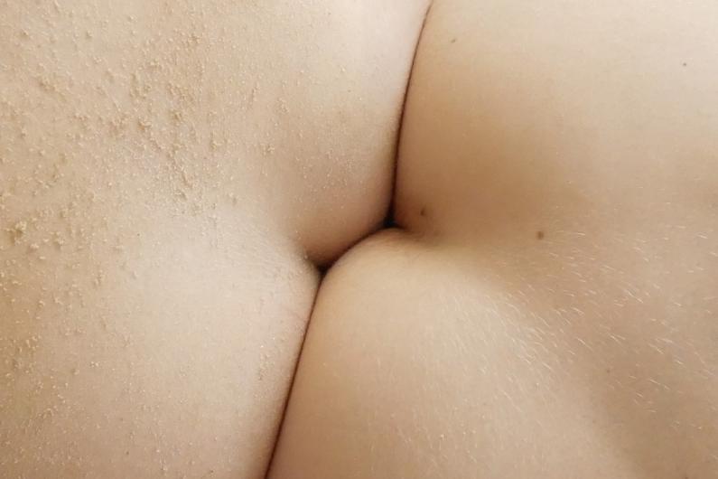 Close-up of two body surfaces pressed together, with grains of sand on the skin.