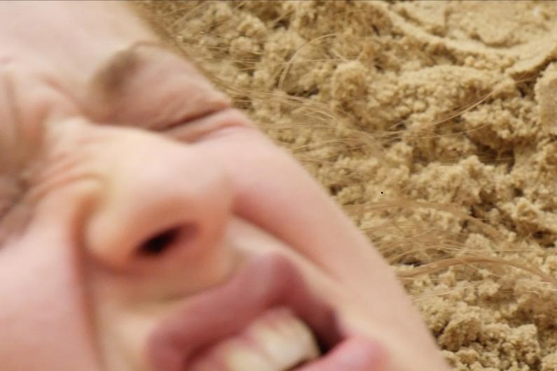 Blurry close-up of a face in the sand, with a tense expression and squinted eyes.