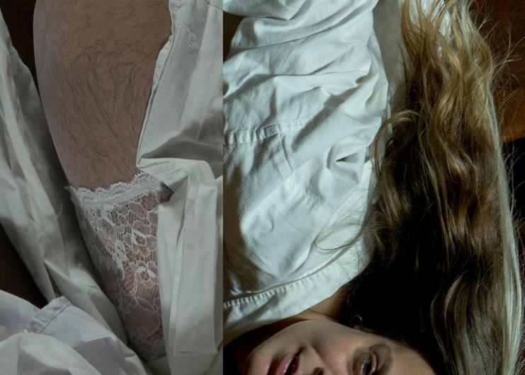 A person lies on white fabric, their face partly visible. A thigh in lace stockings with body hair is shown.