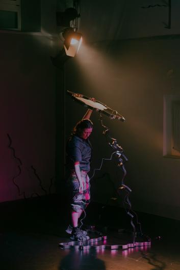 A person stands beneath a warmly lit wooden instrument hanging from the ceiling and gently touches it.