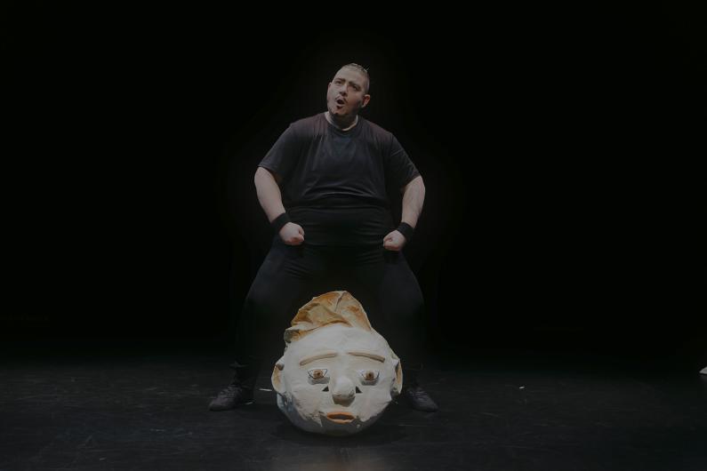 Person in a black outfit stands with clenched fists over a large mask on the ground.