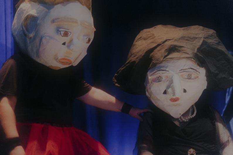 Close-up of two masked figures, one placing a comforting hand on the other's shoulder.
