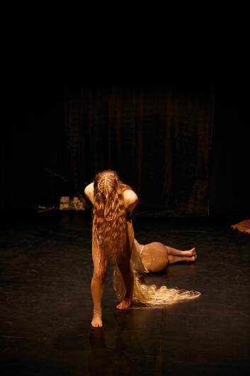 A performer with long, loose hair pulls a reclining person across the stage behind him.