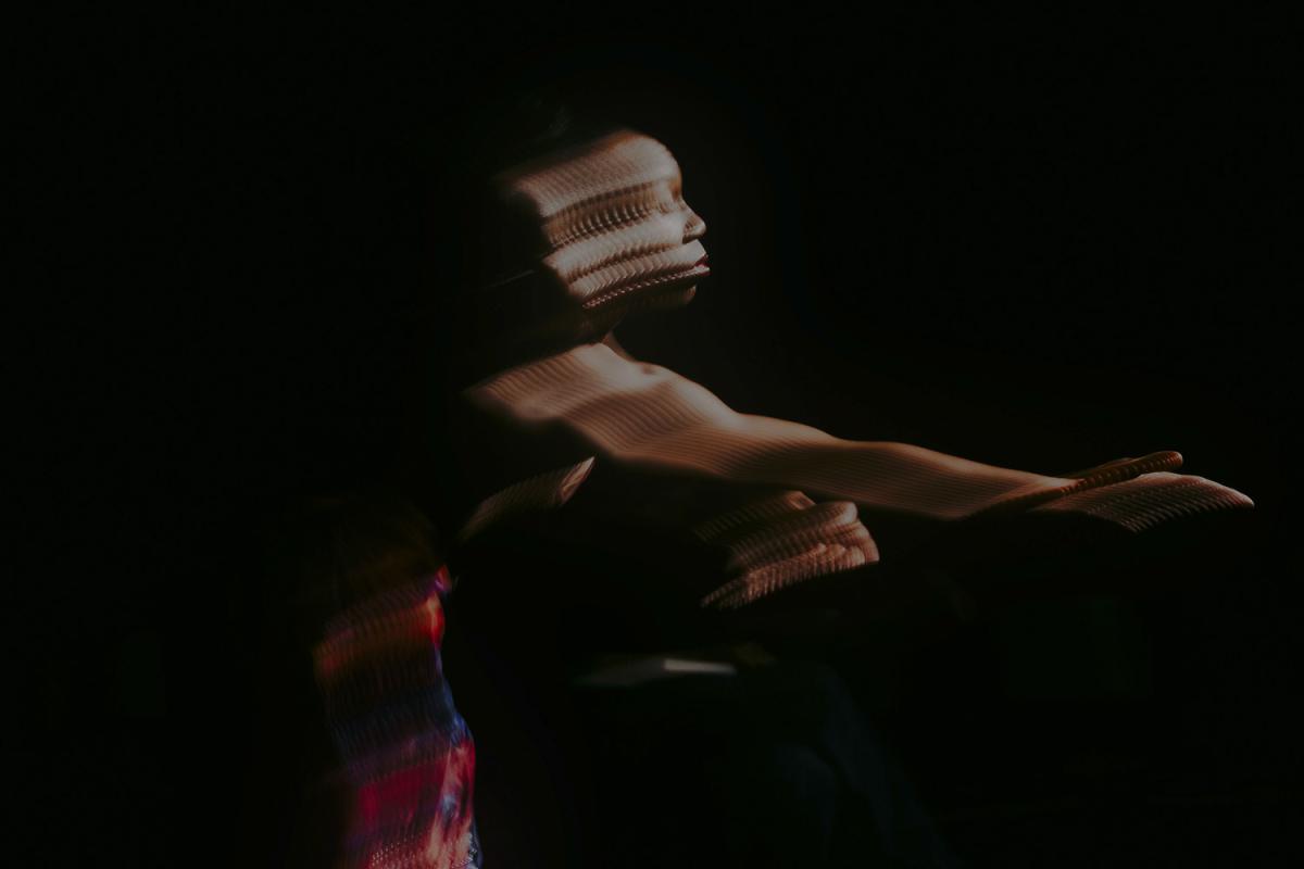 A dancer in a dark setting, his body distorted and layered multiple times by a light projection.
