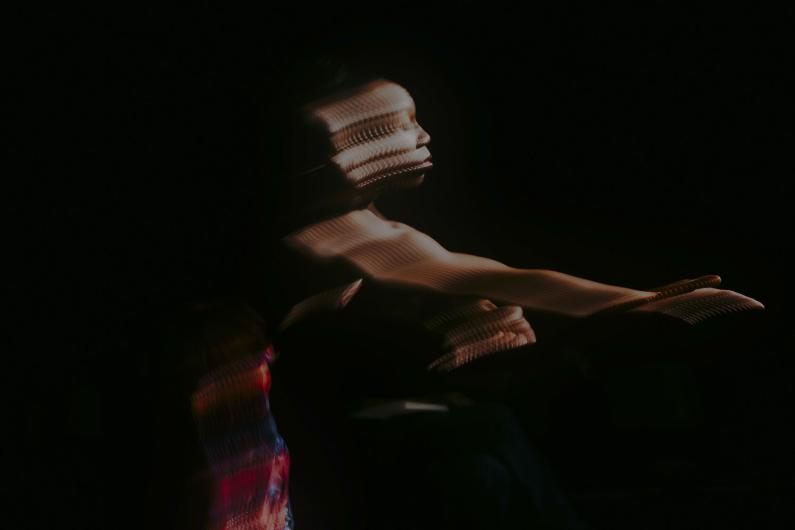 A dancer in a dark setting, his body distorted and layered multiple times by a light projection.