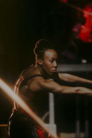 A dancer with a focused expression extends her arms in a powerful dance move as light beams cut through the space.