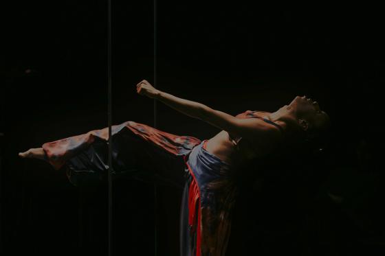 A dancer appears to be floating horizontally in the darkness with her back arched. She only has one leg on the ground, the other is stretched out.