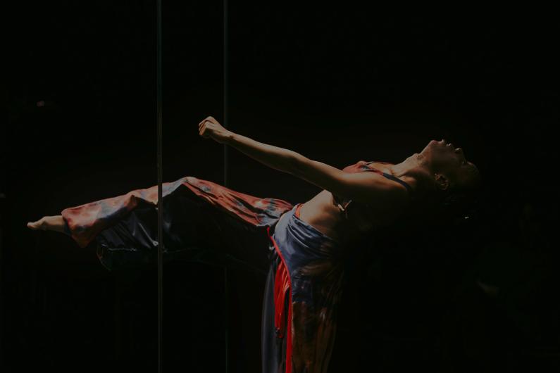 A dancer appears to be floating horizontally in the darkness with her back arched. She only has one leg on the ground, the other is stretched out.