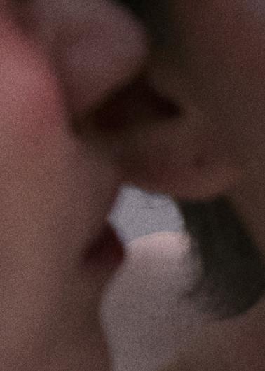 A highly magnified, grainy close-up of two faces almost touching. Their lips are slightly parted, suggesting an intimate and sensual moment.