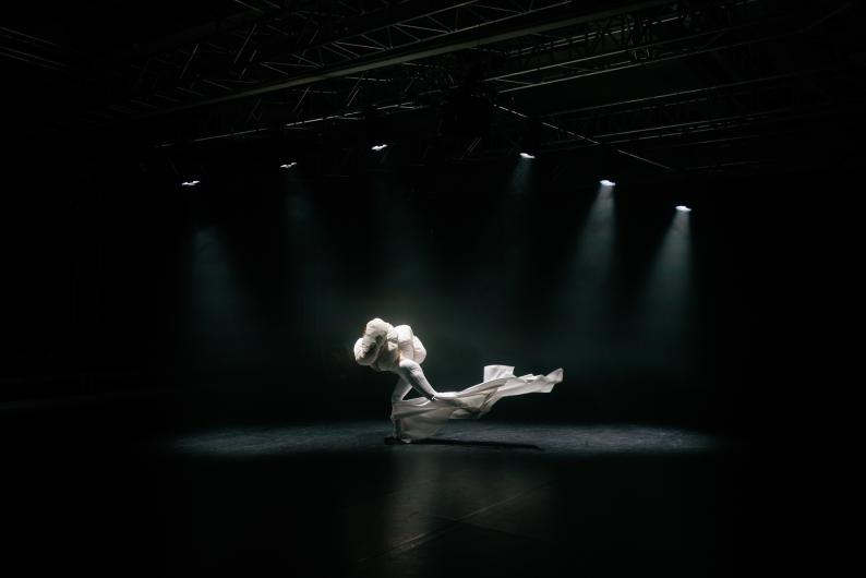Dancer in a white, flowing costume twirls across the stage under dramatic lighting.