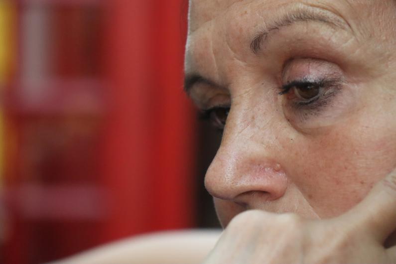 Close-up of a woman’s face with a thoughtful expression. The image focuses mainly on her eyes, forehead, and nose. The background is blurred in shades of red and yellow.
